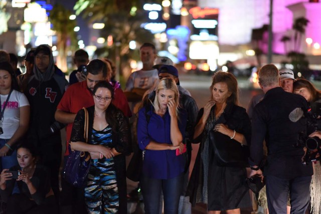 Mourners look on at a makeshift memorial near the Mandalay Hotel on the Las Vegas Strip, in Las Vegas, Nevada on October 3, 2017, after a gunman killed 58 people and wounded more than 500 others, before taking his own life, when he opened fire from a hotel on a country music festival. Police said the gunman, a 64-year-old local resident named as Stephen Paddock, had been killed after a SWAT team responded to reports of multiple gunfire from the 32nd floor of the Mandalay Bay, a hotel-casino next to the concert venue. / AFP PHOTO / Robyn Beck