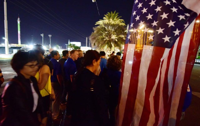 People look on near a US national flag at a makeshift memorial near the Mandalay Hotel on the Las Vegas Strip, in Las Vegas, Nevada on October 3, 2017, after a gunman killed 58 people and wounded more than 500 others, before taking his own life, when he opened fire from a hotel on a country music festival. Police said the gunman, a 64-year-old local resident named as Stephen Paddock, had been killed after a SWAT team responded to reports of multiple gunfire from the 32nd floor of the Mandalay Bay, a hotel-casino next to the concert venue. / AFP PHOTO / Robyn Beck