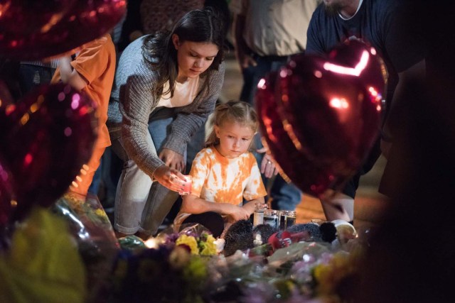 A woman places a candle as a young girl looks on at a makeshift memorial near the Mandalay Hotel on the Las Vegas Strip, in Las Vegas, Nevada on October 3, 2017, after a gunman killed 58 people and wounded more than 500 others, before taking his own life, when he opened fire from a hotel on a country music festival. Police said the gunman, a 64-year-old local resident named as Stephen Paddock, had been killed after a SWAT team responded to reports of multiple gunfire from the 32nd floor of the Mandalay Bay, a hotel-casino next to the concert venue. / AFP PHOTO / Robyn Beck