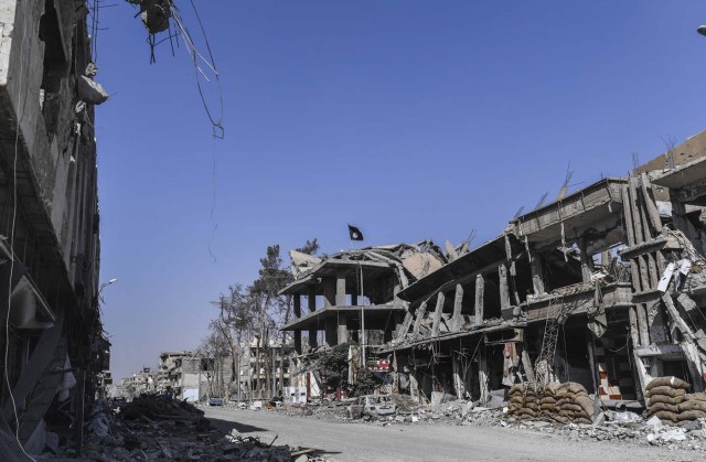An Islamic State (IS) group flag flutters above heavily damaged buildings in Raqa on October 21, 2017, after a Kurdish-led force expelled the jihadists from the northern Syrian city. The US-backed Syrian Democratic Forces officially announced Raqa's capture at a ceremony in the city's stadium on October 20 but said mines left behind by IS made it too dangerous for residents to return home. / AFP PHOTO / BULENT KILIC