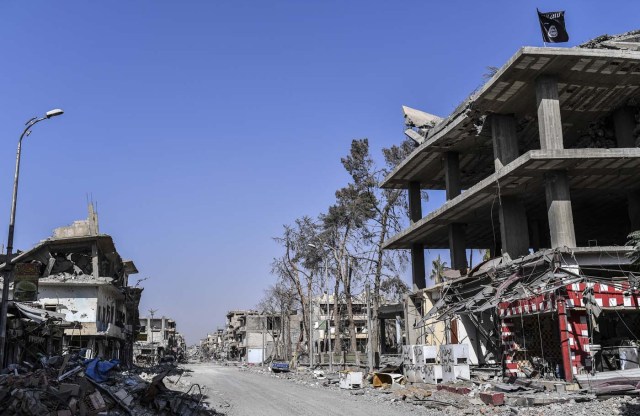 An Islamic State (IS) group flag flutters above heavily damaged buildings in Raqa on October 21, 2017, after a Kurdish-led force expelled the jihadists from the northern Syrian city. The US-backed Syrian Democratic Forces officially announced Raqa's capture at a ceremony in the city's stadium on October 20 but said mines left behind by IS made it too dangerous for residents to return home. / AFP PHOTO / BULENT KILIC