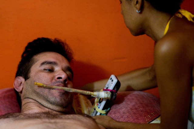 Ana Barrios (R) helps his quadriplegic husband Marco Guillen, to use a stick to dial the TV remote with his mouth at their house in Barquisimeto, Lara state, Venezuela on October 23, 2017. Marco Guillen became quadriplegic in an accident twelve years ago, amid Venezuela's deep economical crisis he desperately asks President Maduro's government to help him to live with dignity, meeting his medical necessities otherwise he pleads for euthanasia. / AFP PHOTO / FEDERICO PARRA / TO GO WITH AFP STORY by MARGIONI BERMUDEZ