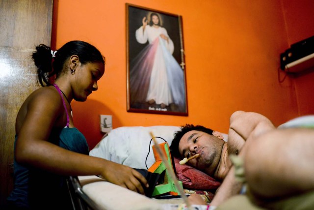Daikellys Mosquera (L), 13, helps his quadriplegic dad Marco Guillen, to use a stick to dial the cellphone with his mouth at their house in Barquisimeto, Lara state, Venezuela on October 23, 2017. Marco Guillen became quadriplegic in an accident twelve years ago, amid Venezuela's deep economical crisis he desperately asks President Maduro's government to help him to live with dignity, meeting his medical necessities otherwise he pleads for euthanasia. / AFP PHOTO / FEDERICO PARRA / TO GO WITH AFP STORY by MARGIONI BERMUDEZ