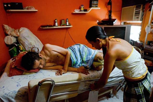 Ana Barrios (R), takes care of her quadriplegic husband Marco Guillen, at their house in Barquisimeto, Lara state, Venezuela on October 23, 2017. Marco Guillen became quadriplegic in an accident twelve years ago, amid Venezuela's deep economical crisis he desperately asks President Maduro's government to help him to live with dignity, meeting his medical necessities otherwise he pleads for euthanasia. / AFP PHOTO / FEDERICO PARRA / TO GO WITH AFP STORY by MARGIONI BERMUDEZ
