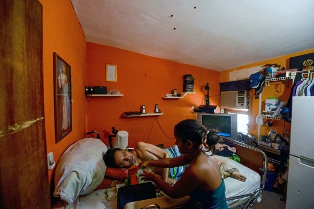 Daikellys Mosquera (R), 13, helps his quadriplegic dad Marco Guillen, to drink water at their house in Barquisimeto, Lara state, Venezuela on October 23, 2017. Marco Guillen became quadriplegic in an accident twelve years ago, amid Venezuela's deep economical crisis he desperately asks President Maduro's government to help him to live with dignity, meeting his medical necessities otherwise he pleads for euthanasia. / AFP PHOTO / FEDERICO PARRA / TO GO WITH AFP STORY by MARGIONI BERMUDEZ
