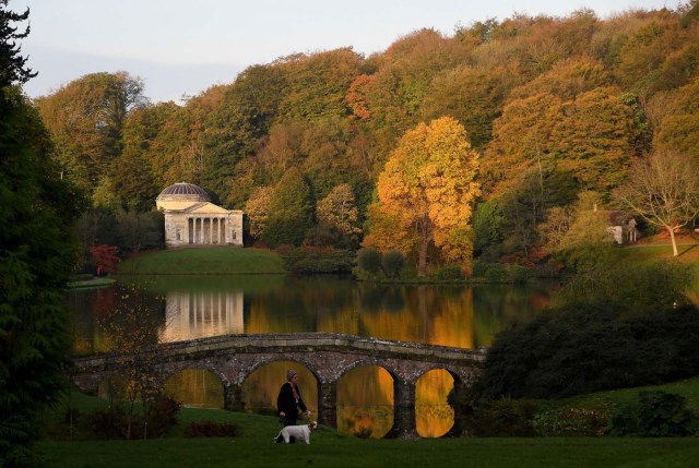 Autumn colours are seen in the early morning sunshine as a woman walks her dog at Stourhead gardens in Wiltshire, south west Britain, October 17, 2017. REUTERS/Toby Melville