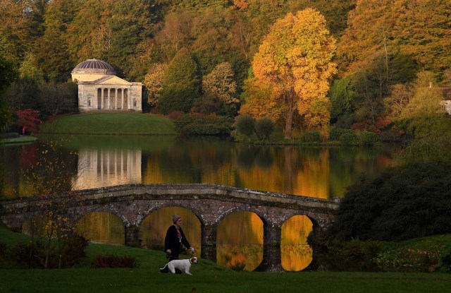 Autumn colours are seen in the early morning sunshine as a woman walks her dog at Stourhead gardens in Wiltshire, south west Britain, October 17, 2017. REUTERS/Toby Melville