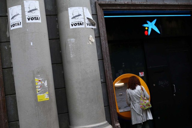 A woman uses a Caixa Bank ATM machine next to signs that read "Vote", on the day of a protest against the transfer of the bank's headquarters out of Barcelona, Spain, October 20, 2017. REUTERS/Ivan Alvarado