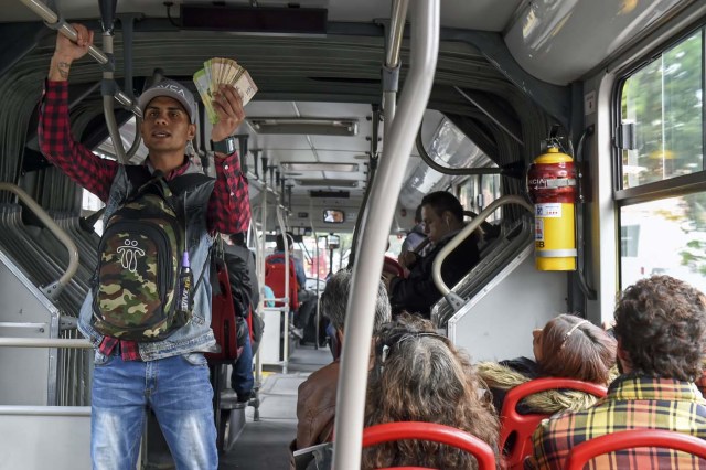 Venezuelan national Jhonger Pina, 25, sells candies and shows Bolivar bills as a curiosity to passengers, in exchange for local coins on a bus in Bogota, on October 26, 2017. Up to October 2017 there were 470,000 Venezuelans in Colombia, who left their country to escape the hardship and violence of its economic and political crisis. / AFP PHOTO / Raul Arboleda / TO GO WITH AFP STORY by Daniela QUINTERO and Santiago TORRADO