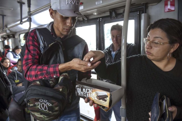 Venezuelan national Jhonger Pina, 25, sells candies and shows Bolivar bills as a curiosity to passengers, in exchange for local coins on a bus in Bogota, on October 26, 2017. Up to October 2017 there were 470,000 Venezuelans in Colombia, who left their country to escape the hardship and violence of its economic and political crisis. / AFP PHOTO / Raul Arboleda / TO GO WITH AFP STORY by Daniela QUINTERO and Santiago TORRADO