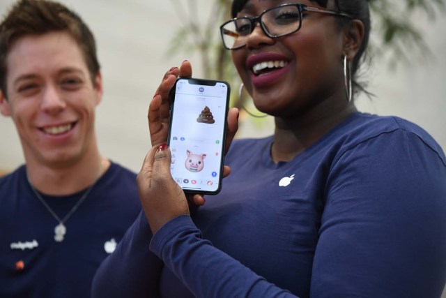 A member of Apple staff pose with a new Apple iPhone X smartphone showing new emoji features in Apple's Regent Street store in central London on November 3, 2017 after it opened for the first sales of the new smartphone. Apple's flagship iPhone X hit stores on November 3, as the world's most valuable company predicted bumper sales despite the handset's eye-watering price tag and celebrated a surge in profits. The device features facial recognition, cordless charging and an edge-to-edge screen made of organic light-emitting diodes used in high-end televisions. It marks the 10th anniversary of the first iPhone release and is released in about 50 markets around the world. / AFP PHOTO / Chris J Ratcliffe