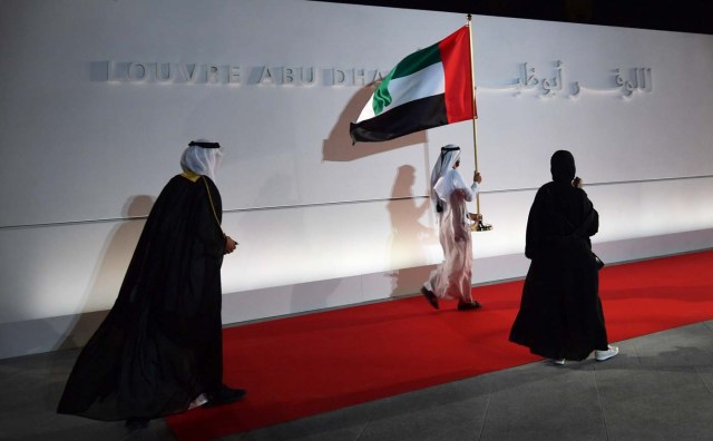 An Emirari man walks carrying his national flag at the entrance of the Louvre Abu Dhabi Museum on November 8, 2017 prior to its inauguration on Saadiyat island in the Emirati capital. More than a decade in the making, the Louvre Abu Dhabi is opening its doors bringing the famed name to the Arab world for the first time. / AFP PHOTO / Giuseppe CACACE