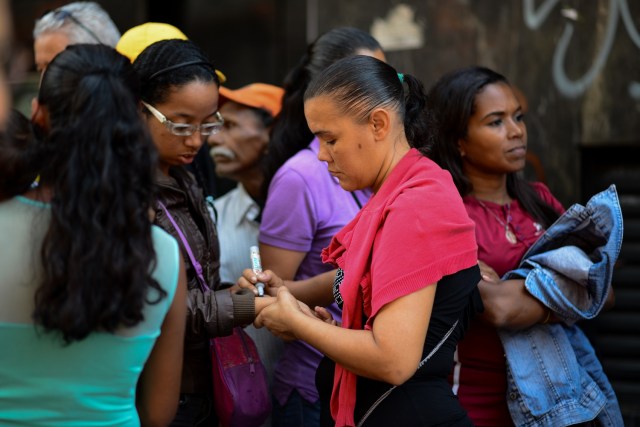 A woman writes numbers on people's arms so they know what order they came in, as they queue outside a supermarket in Caracas to buy basic foodstuffs and household products on November 10, 2017. In crisis-stricken Venezuela, the cost of the basic basket of goods soared to nearly 2.7 million bolivars in September, the equivalent of six minimum monthly wages. / AFP PHOTO / FEDERICO PARRA