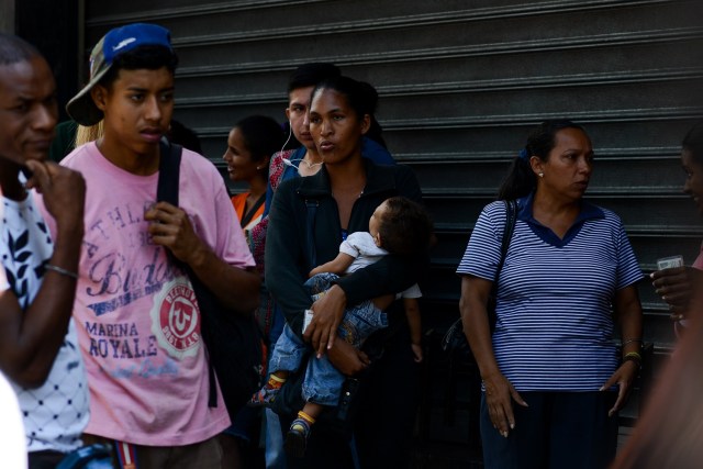 A woman holds her baby while queuing outside a supermarket in Caracas to buy basic food and household items on November 10, 2017. In crisis-stricken Venezuela, the cost of the basic basket of goods soared to nearly 2.7 million bolivars in September, the equivalent of six minimum monthly wages. / AFP PHOTO / FEDERICO PARRA