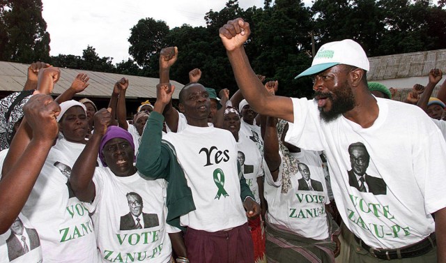 (FILES) This file photo taken on April 14, 2000 shows a leader of the war veterans, Chino Timba (R), supporting squatters wearing electoral shirts, in the Gelnara farm occupied since April 7, outside Harare.  Robert Mugabe resigned as president of Zimbabwe on November 21, 2017, parliament speaker Jacob Mudenda told lawmakers, ending a 37-year rule defined by brutality and economic collapse. "I Robert Gabriel Mugabe in terms of section 96 of the constitution of Zimbabwe hereby formally tender my resignation... with immediate effect," said speaker Mudenda, reading the letter. / AFP PHOTO / ALEXANDER JOE