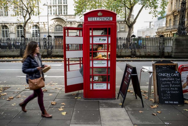Fouad Choaibi works inside a red telephone box from which he runs a smartphone repair shop on Southhampton Row, in central London on October 20, 2017. Facing extinction due to ubiquitous mobile phones, Britain's classic red telephone boxes are being saved from death row by ingenious conversions into all sorts of new uses. / AFP PHOTO / Tolga Akmen / TO GO WITH AFP STORY 'Britain-heritage-business' by Martine PAUWELS