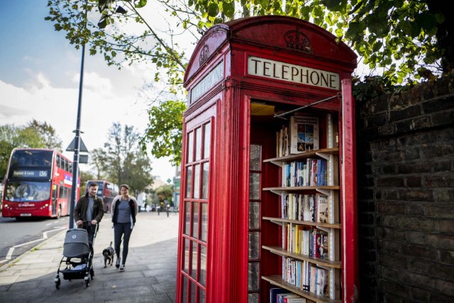Pedestrians walk past a red telephone box turned into a book exchange library on Lewisham Way, in south London on October 21, 2017. Facing extinction due to ubiquitous mobile phones, Britain's classic red telephone boxes are being saved from death row by ingenious conversions into all sorts of new uses. / AFP PHOTO / AFP PHOTO AND Tolga Akmen / TOLGA AKMEN / TO GO WITH AFP STORY 'Britain-heritage-business' by Martine PAUWELS