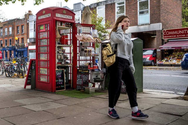 A pedestrian walks past a coffee shop run by Umar Khalid (unseen) in a red telephone box in Hampstead Heath, north London on October 20, 2017. Facing extinction due to ubiquitous mobile phones, Britain's classic red telephone boxes are being saved from death row by ingenious conversions into all sorts of new uses. / AFP PHOTO / Tolga Akmen / TO GO WITH AFP STORY 'Britain-heritage-business' by Martine PAUWELS
