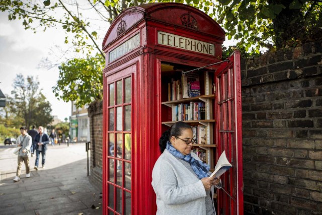Local resident, Patsy Ari browses the books at a red telephone box turned into a book exchange library on Lewisham Way, in south London on October 21, 2017. Facing extinction due to ubiquitous mobile phones, Britain's classic red telephone boxes are being saved from death row by ingenious conversions into all sorts of new uses. / AFP PHOTO / TOLGA AKMEN / TO GO WITH AFP STORY 'Britain-heritage-business' by Martine PAUWELS