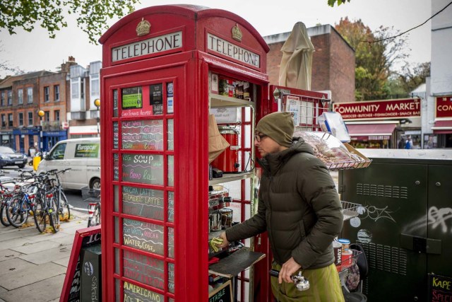 Umar Khalid cleans the red telephone box from which he runs a coffee shop in Hampstead Heath, north London on October 20, 2017. Facing extinction due to ubiquitous mobile phones, Britain's classic red telephone boxes are being saved from death row by ingenious conversions into all sorts of new uses. / AFP PHOTO / Tolga Akmen / TO GO WITH AFP STORY 'Britain-heritage-business' by Martine PAUWELS