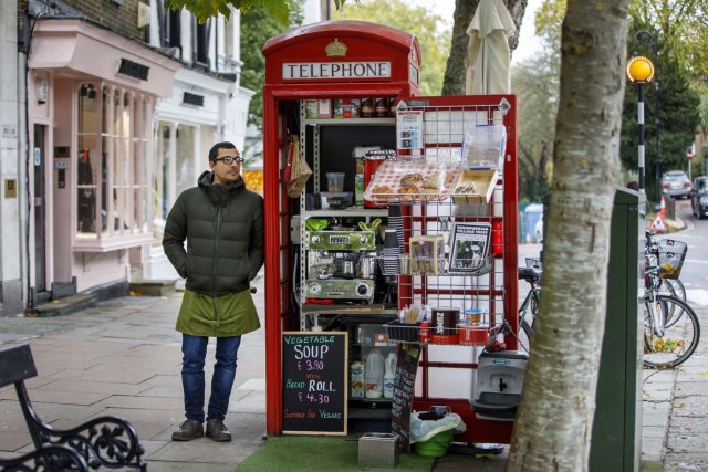 Umar Khalid poses outside the red telephone box from which he runs a coffee shop in Hampstead Heath, north London on October 20, 2017. Facing extinction due to ubiquitous mobile phones, Britain's classic red telephone boxes are being saved from death row by ingenious conversions into all sorts of new uses. / AFP PHOTO / Tolga Akmen / TO GO WITH AFP STORY 'Britain-heritage-business' by Martine PAUWELS