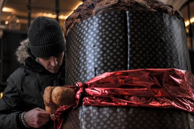 A baker decorates a giant "Panettone" on December 17, 2017 in the Vittorio Emanuele II gallery in Milan. The Panettone, a typical brioche of Christmas in the Lombardy region, is traditionally stuffed with raisins, candied fruits and citrus zest.  / AFP PHOTO / MARCO BERTORELLO