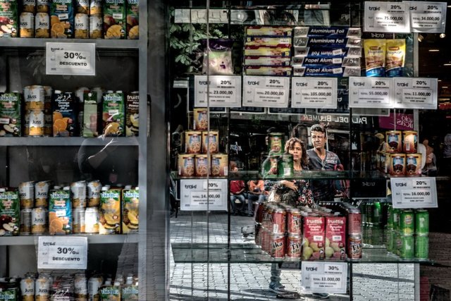Una pareja ve los nuevos precios de una tienda en Caracas desde el aparador. Credit Meridith Kohut para The New York Times