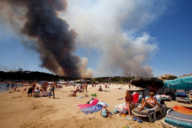 Smoke fills the sky above a burning hillside as tourists relax on the beach in Bormes-les-Mimosas, in the Var department, France, July 26, 2017.    REUTERS/Jean-Paul Pelissier/File Photo      SEARCH "POY GLOBAL" FOR THIS STORY. SEARCH "REUTERS POY" FOR ALL BEST OF 2017 PACKAGES.    TPX IMAGES OF THE DAY