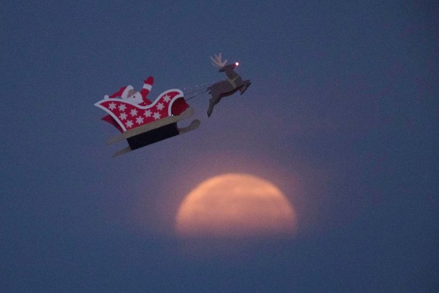 A 10-foot long remote controlled flying Santa makes a test flight past a setting moon over the ocean in Carlsbad, California, U.S., December 3, 2017. REUTERS/Mike Blake