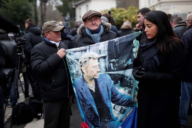 French fans Andre Thibert, left, and Andre Duval display a poster of late French singer and actor Johnny Hallyday as they talk to journalists in Marnes-la-Coquette near Paris, France December 6, 2017. REUTERS/Benoit Tessier