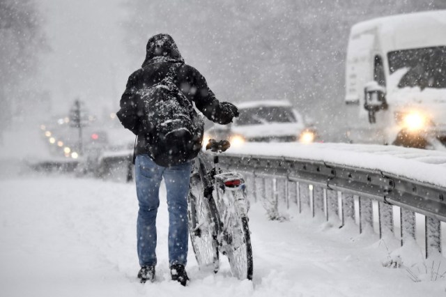 A man walks alongside his snow-covered bicycle in Kontich, near Antwerp, as cold temperatures sweep across Belgium on December 11, 2017.  / AFP PHOTO / BELGA AND Belga / DIRK WAEM / Belgium OUT