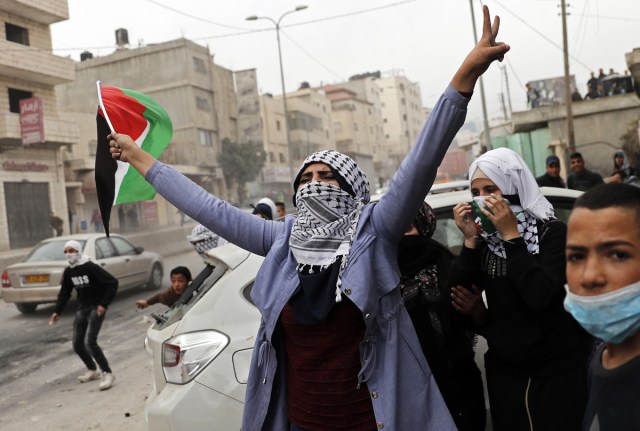 A female Palestinian protestor waves her national flag during clashes with Israeli security forces near the Qalandia checkpoint in the Israeli occupied West Bank on December 20, 2017 as protests continue following the US president's controversial recognition of Jerusalem as Israel's capital. / AFP PHOTO / THOMAS COEX