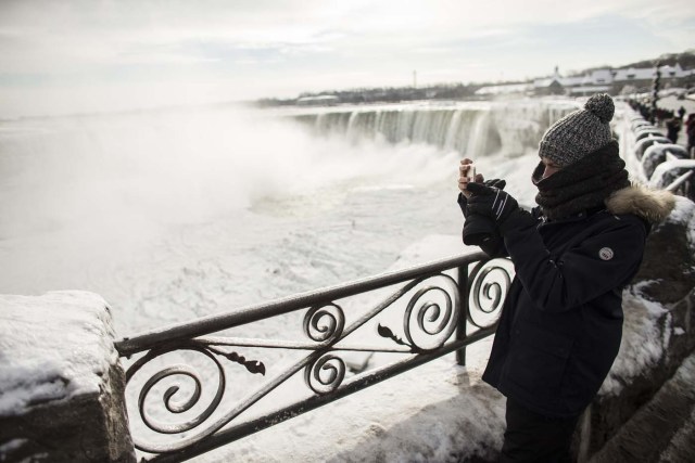 A tourist takes photos of the Horseshoe Falls in Niagara Falls, Ontario on January 3, 2018. The cold snap which has gripped much of Canada and the United States has nearly frozen over the American side of the falls. / AFP PHOTO / Geoff Robins