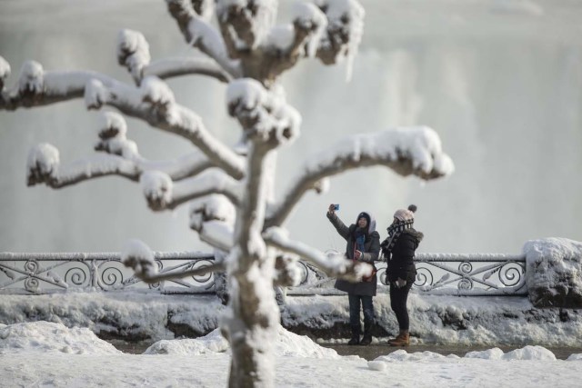 Tourists take photos of the Horseshoe Falls in Niagara Falls, Ontario on January 3, 2018. The cold snap which has gripped much of Canada and the United States has nearly frozen over the American side of the falls. / AFP PHOTO / Geoff Robins