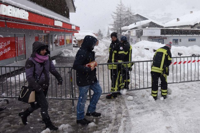 Tourists walk past emergency workers beside the Zermatt train station after heavy snowfall and avalanches trapped more than 13,000 tourists at Zermatt, which is one of Switzerland's most popular ski stations on January 09, 2018. The snow has blocked all roads and the train leading to the resort in the southern Swiss canton of Valais, which was also hit by some power outages. / AFP PHOTO / Mark Ralston