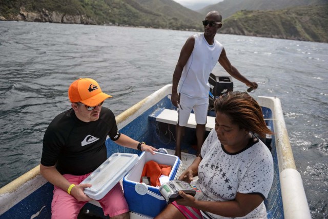 Nancy Rodriguez (R) charges food to a tourist's credit card in a boat, after motoring two km off the coast of Chichiriviche de la Costa, to find an internet signal, some 70 km northwest of Caracas on January 13, 2018. The inhabitants of the village of Chichiriviche de la Costa, which depends on tourism, have come up with an ingenious way to deal with the lack of cash and internet connection. / AFP PHOTO / FEDERICO PARRA