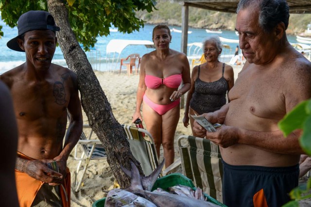 A tourist buys fish on the beach at Chichiriviche de la Costa, some 70 km northwest of Caracas on January 13, 2018. The inhabitants of the village of Chichiriviche de la Costa, which depends on tourism, have come up with an ingenious way to deal with the lack of cash and internet connection. / AFP PHOTO / FEDERICO PARRA