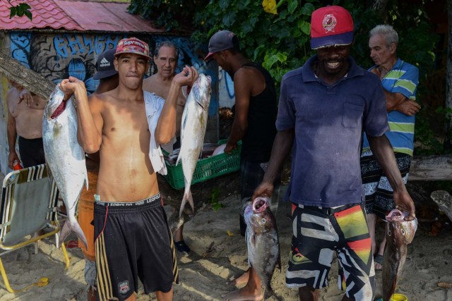 Fishermen carry fish at the beach in Chichiriviche de la Costa, a village some 70 km northwest of Caracas, on January 13, 2018. The inhabitants of the village of Chichiriviche de la Costa, which depends on tourism, have come up with an ingenious way to deal with the lack of cash and internet connection. / AFP PHOTO / FEDERICO PARRA