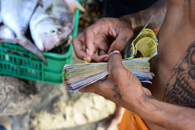 A fisherman counts bills on the beach in the village of Chichiriviche de la Costa, some 70 km northwest of Caracas, on January 13, 2018. The inhabitants of the village of Chichiriviche de la Costa, which depends on tourism, have come up with an ingenious way to deal with the lack of cash and internet connection. / AFP PHOTO / FEDERICO PARRA