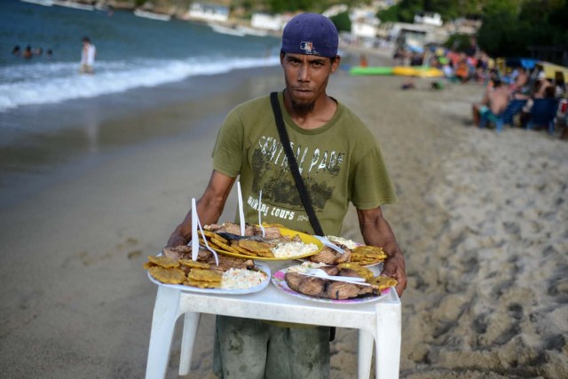 A man carries meals for tourists at the beach of Chichiriviche de la Costa, some 70 km northwest of Caracas on January 13, 2018. The inhabitants of the village of Chichiriviche de la Costa, which depends on tourism, have come up with an ingenious way to deal with the lack of cash and internet connection. / AFP PHOTO / FEDERICO PARRA