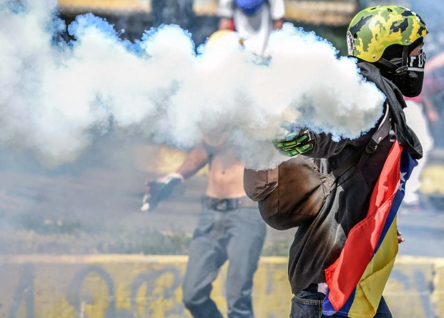 A demonstrator throws a tear gas canister back at the riot police during clashes in Caracas on January 22, 2018 which erupted during a protest to condemn the death of dissident former police officer Oscar Perez - gunned down in a bloody police operation on February 16.  Perez, whose body was buried by the government on January 21 against his family's wishes, was Venezuela's most wanted man since June when he flew a stolen police helicopter over Caracas dropping grenades on the Supreme Court and opening fire on the Interior Ministry.  / AFP PHOTO / Juan BARRETO