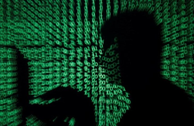 Ilustración fotográfica de la silueta de una persona utilizando un ordenador portátil proyectada sobre una pared iluminada con código binario, mayo 13, 2017. REUTERS/Kacper Pempel/Illustration