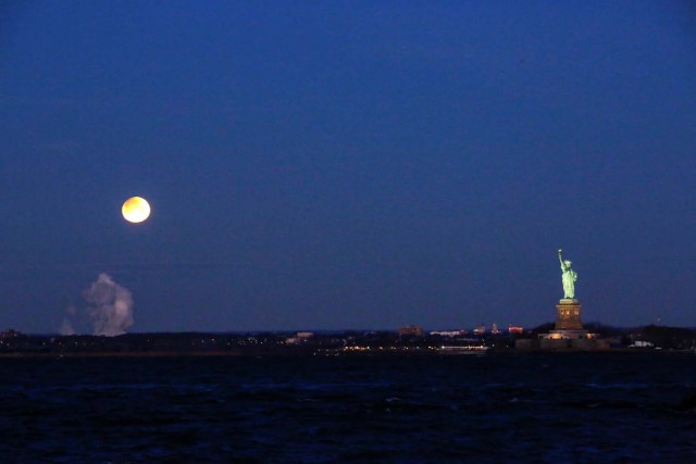 A "Super Blue Blood Moon" sets next to the Statue of Liberty as it is seen from Brooklyn, in New York, U.S., January 31, 2018. REUTERS/Eduardo Munoz
