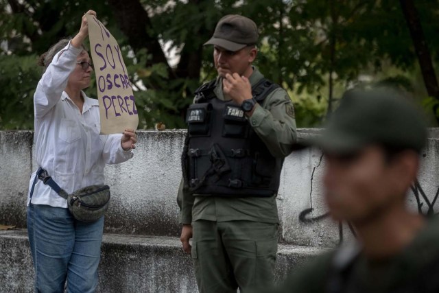 CAR13. CARACAS (VENEZUELA), 17/01/2018.- Una mujer sostiene un cartel en el que se lee "Yo soy Óscar Pérez" frente a miembros de la Guardia Nacional Bolivariana y la Policía Nacional Bolivariana que custodian las inmediaciones de la morgue en donde está cuerpo del exagente Pérez hoy, miércoles 17 de enero de 2018, en Caracas (Venezuela). Decenas de agentes de la Policía Nacional Bolivariana custodian desde la mañana de hoy los alrededores de la principal morgue de Caracas, después de que familiares de Óscar Pérez, el exagente alzado contra el Gobierno chavista quien falleció el lunes, exigieran identificar su cuerpo. EFE/MIGUEL GUTIÉRREZ