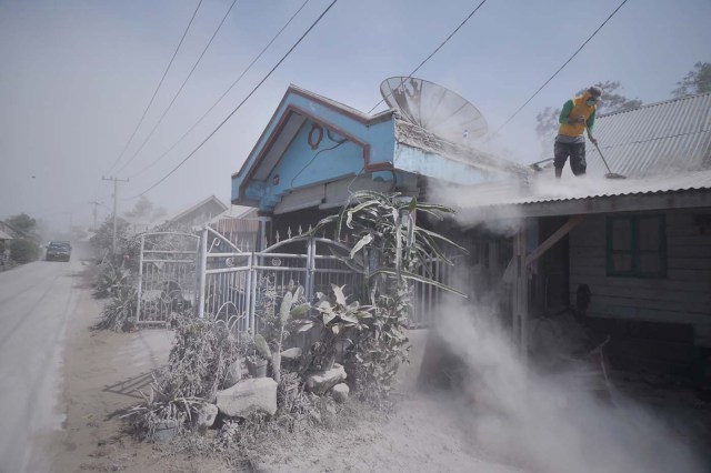 An Indonesian man cleans dust from a roof of a house after Mount Sinabung spewed volcanic ash a day before in Karo, North Sumatra on February 20, 2018. Mount Sinabung volcano erupted on February 19, sending a massive column of ash and smoke some 5,000 metres (16,400 feet)into the air, leaving local villages coated in debris and officials scrambling to hand out face masks to residents. / AFP PHOTO / LANA PRIATNA