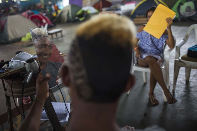 A Venezuelan refugee looks at his new haircut on a piece of mirror, inside a shelter in the city of Boa Vista, Roraima, Brazil, on February 24, 2018. When the Venezuelan migratory flow exploded in 2017 the city of Boa Vista, the capital of Roraima, 200 kilometres from the Venezuelan border, began to organise shelters as people started to settle in squares, parks and corners of this city of 330,000 inhabitants of which 10 percent is now Venezuelan. / AFP PHOTO / MAURO PIMENTEL