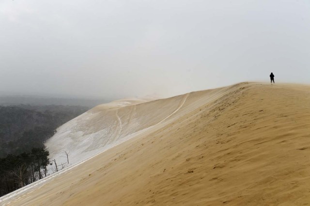 A man walks on the partially snow covered Pilat (or Pyla) sand dune after snow fall on February 28, 2018 in La Teste-de-Buch, southwestern France. Europe remained on February 28 gripped by a blast of Siberian weather, accounting for at least 24 deaths and carpeting palm-lined Mediterranean beaches in snow. / AFP PHOTO / NICOLAS TUCAT