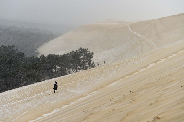 A woman walks on the partially snow covered Pyla sand dune during snow fall on February 28, 2018 in La Teste-de-Buch, southwestern France. Europe remained on February 28 gripped by a blast of Siberian weather, accounting for at least 24 deaths and carpeting palm-lined Mediterranean beaches in snow. / AFP PHOTO / NICOLAS TUCAT