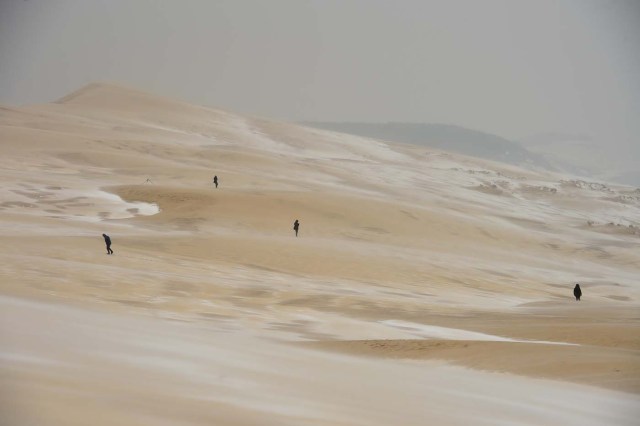 People walk on the partially snow covered Pilat (or Pyla) sand dune after snow fall on February 28, 2018 in La Teste-de-Buch, southwestern France. Europe remained on February 28 gripped by a blast of Siberian weather, accounting for at least 24 deaths and carpeting palm-lined Mediterranean beaches in snow. / AFP PHOTO / Nicolas TUCAT