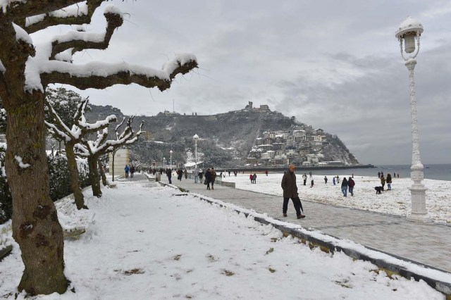 People walk along the beach covered with snow after a heavy snowfall in San Sebastian, northern Spain, on February 28, 2018. School was cancelled across swathes of Europe as a blast of Siberian weather dubbed the "Beast from the East" kept the mercury far below zero. / AFP PHOTO / ANDER GILLENEA